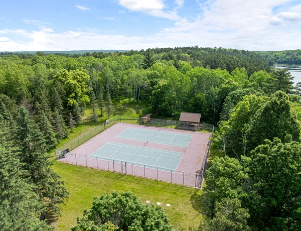 Aerial view of two tennis courts surrounded by dense trees, the lake can be seen in the distance