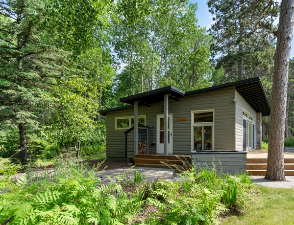 The exterior of Garden cottage with a sloped roof, large windows, gray siding, and long patio