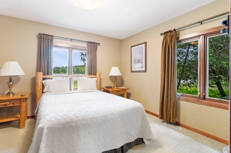 A bedroom at petite cottage with large windows looking out into the trees, a single bed with a white bedspread, and two nightstands