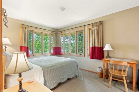 A bedroom at South cottage with two large corner windows, a single bed, and a desk