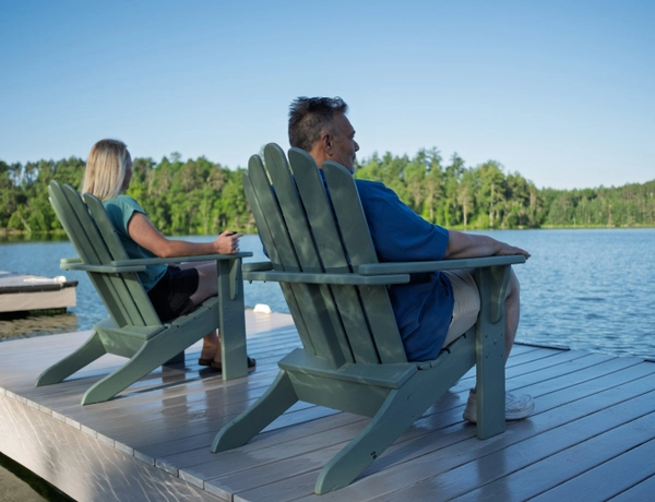 Two people sitting on chairs on the dock looking out towards the lake