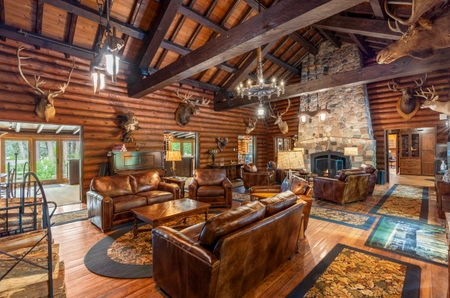 A shared community room with leather couches, a fireplace, chandelier lighting, and several animals mounted on the walls