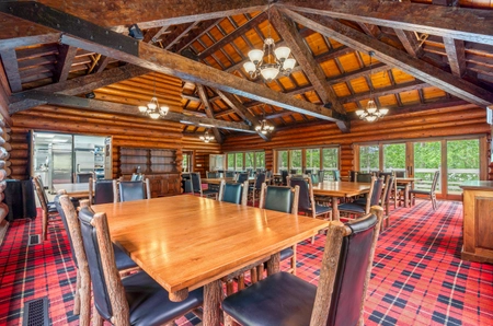 The dining room of the main lodge with red gingham carpet, long wooden tables, and black chairs